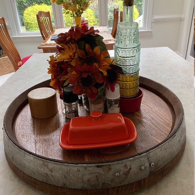 A cozy dining table setting featuring a rustic wooden lazy Susan adorned with a vibrant bouquet, colorful glass bottles, and kitchen condiments, creating a warm, inviting atmosphere.