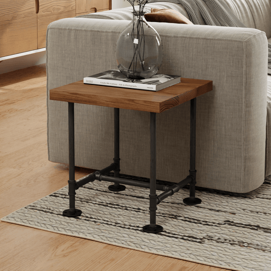 Contemporary side table with a wooden top and industrial-style metal pipes as legs, accessorized with a glass vase and book, set against a cozy beige sofa and textured rug. Ideal for a modern living space.