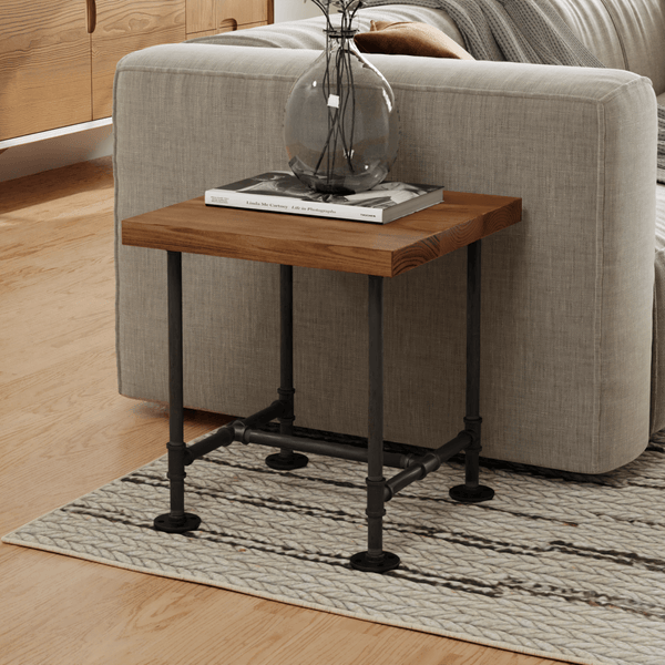 Contemporary side table with a wooden top and industrial-style metal pipes as legs, accessorized with a glass vase and book, set against a cozy beige sofa and textured rug. Ideal for a modern living space.