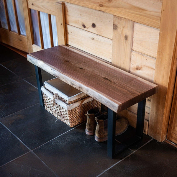 Rustic wooden entryway bench with metal legs, featuring a wicker storage basket and leather boots underneath, against a pine wall. Cozy and practical for home interiors. #HomeDecor #RusticFurniture