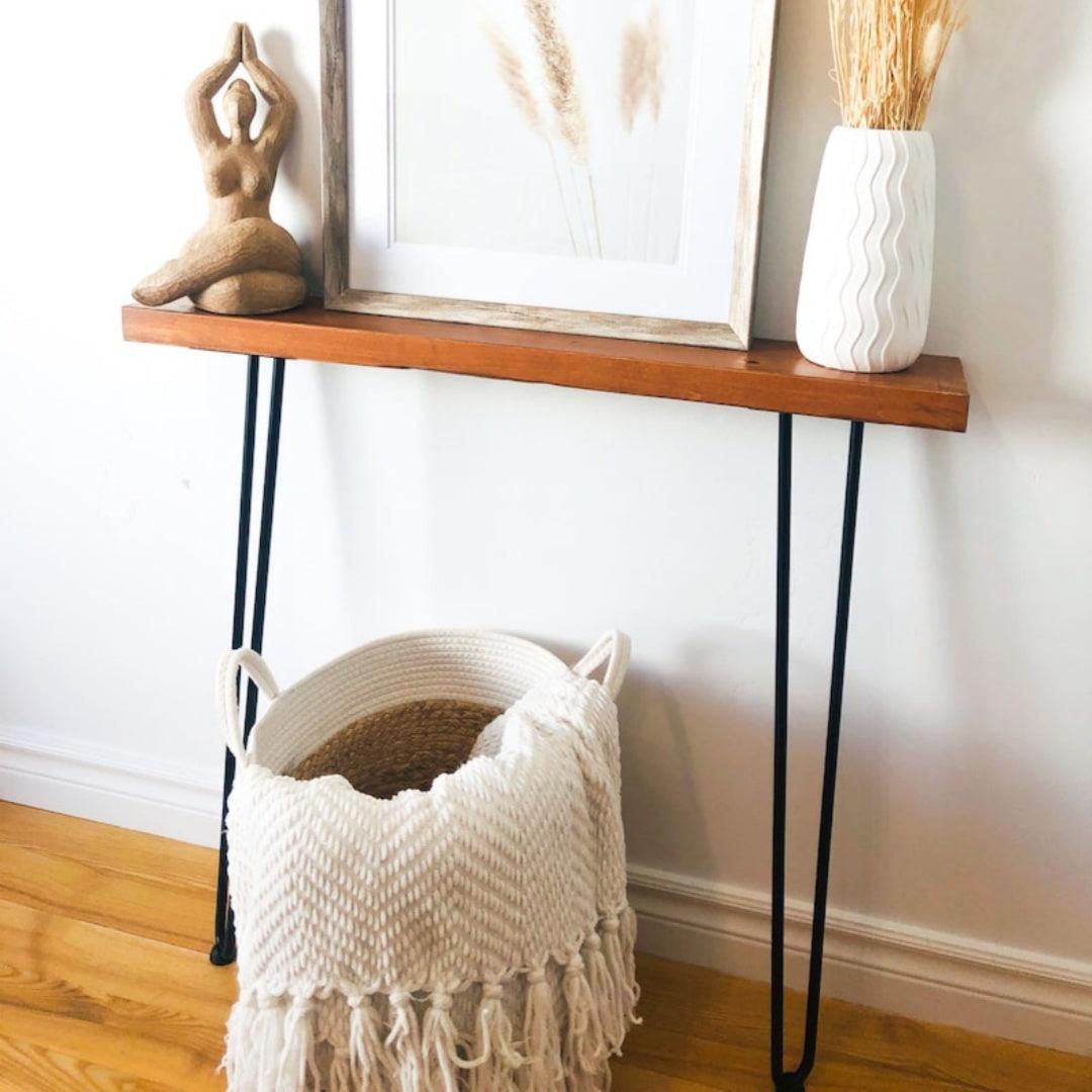 Minimalist home interior with wooden shelf, woven basket with throw blanket, sculpture, framed art, and vase with dried grasses, showcasing a serene and cozy decor style. Ideal for modern living space inspiration.